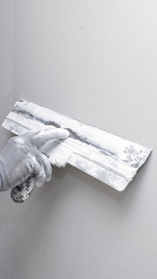 A hand using a putty knife to spread joint compound on a wall.